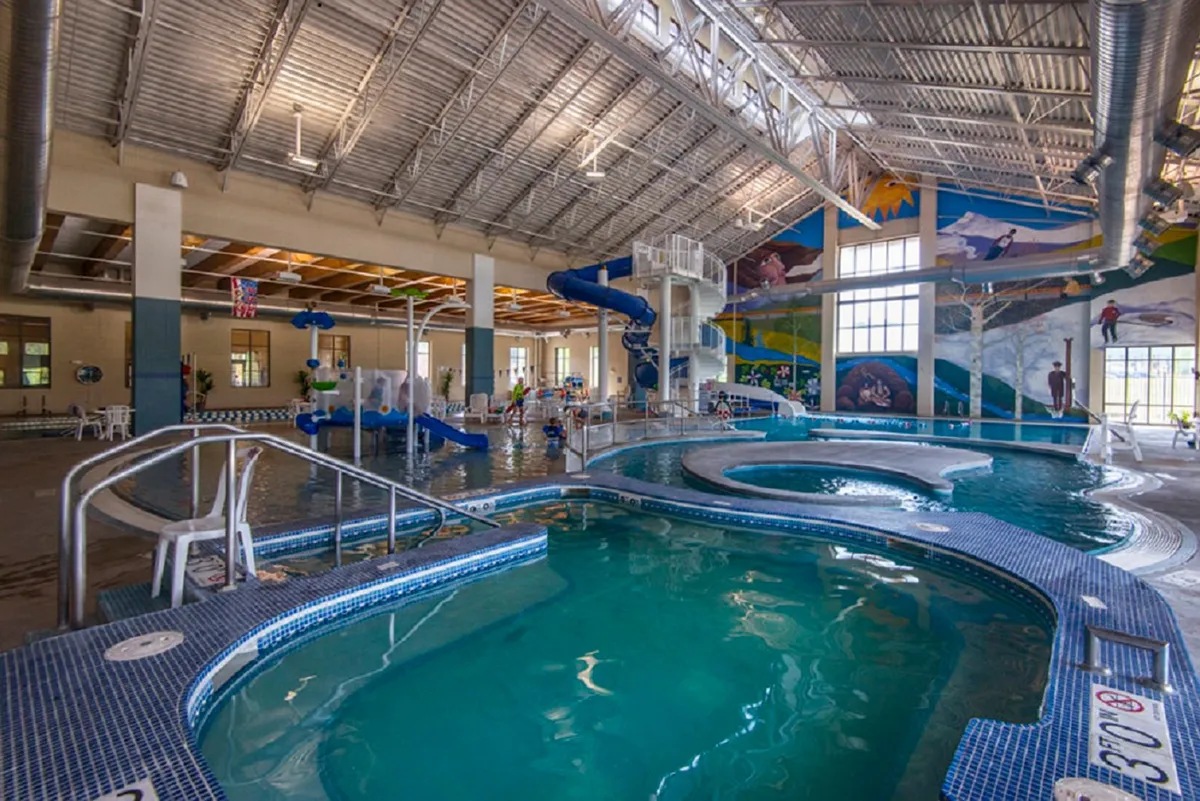 An energetic interior scene featuring children playing and swimming in a pool area with water slides and colorful murals. The joyful atmosphere is perfect for families seeking fun and relaxation after a day outdoors.