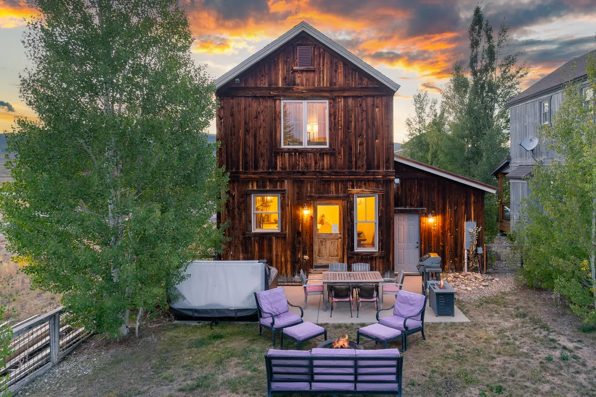 A cozy wooden house with an inviting fire pit surrounded by outdoor seating, set against a glowing sunset sky. The area is perfect for family gatherings, sharing stories, or stargazing after a day of adventure. The scene evokes warmth, relaxation, and togetherness in a scenic natural setting.