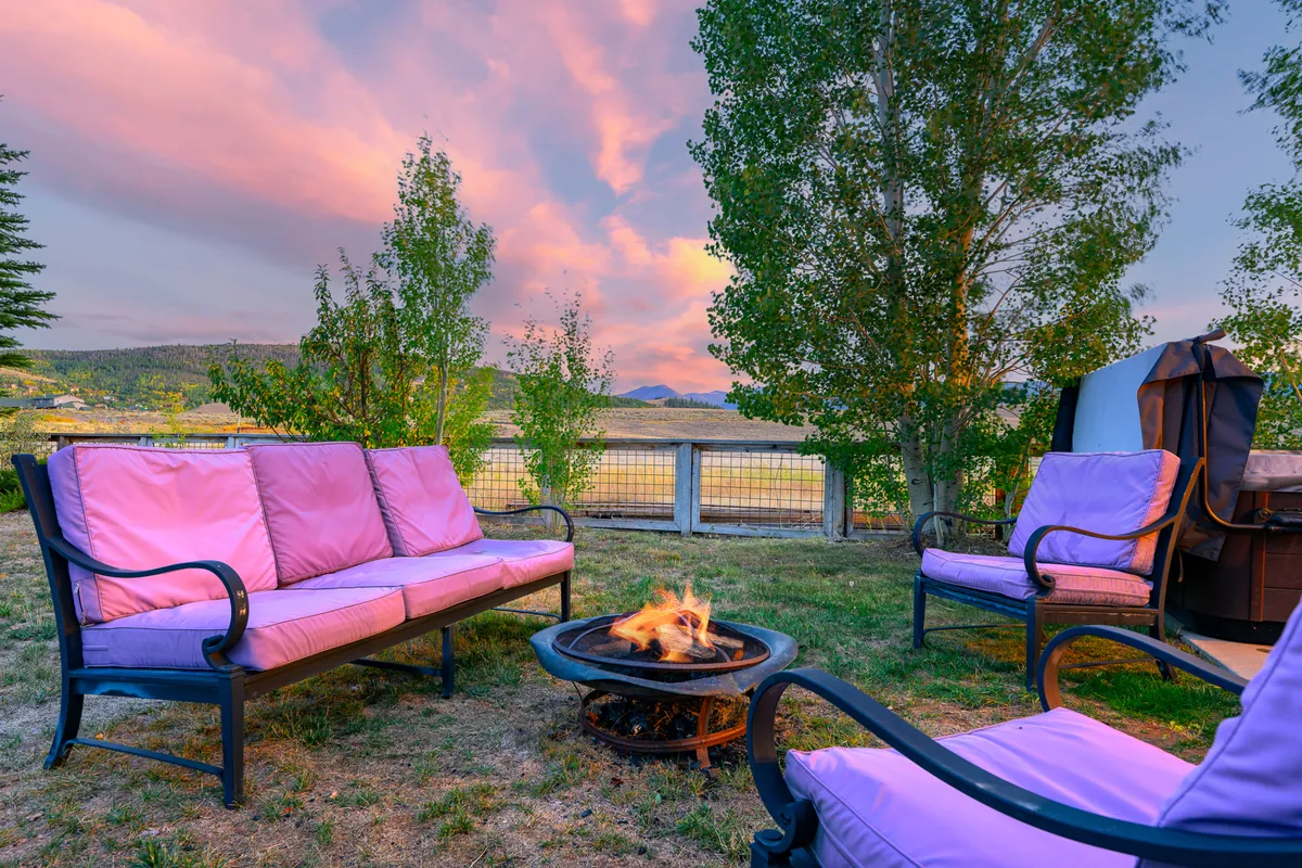 A cozy exterior seating area with pink couches around a fire pit, set against a beautiful landscape. The scene is designed for gathering, relaxing, and sharing moments—ideal for guests with pets seeking comfort after outdoor adventures.
