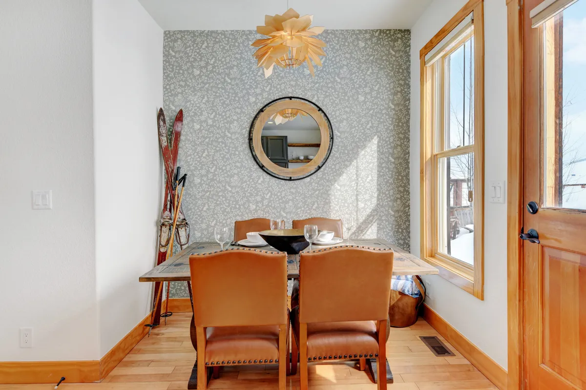A stylish dining area with a spacious table, eye-catching chandelier, wall mirror, and decorative skis reflecting mountain adventures. A large window brings in natural light, while the table setting invites group meals and celebrations.